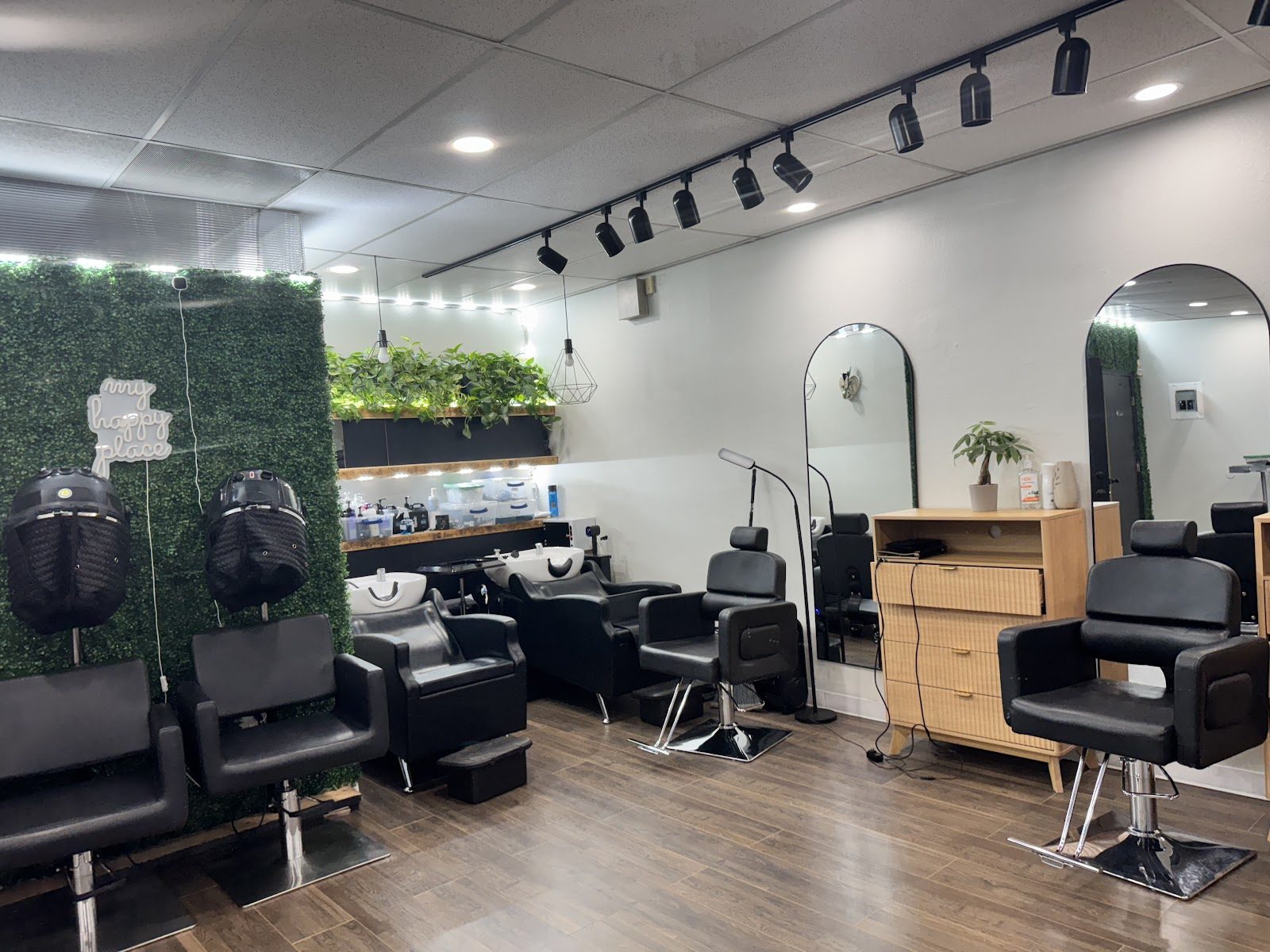 The salon floor: black styling chairs, wood stations and a green living wall under track lights